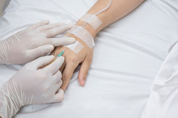 High angle view of doctor's hand injects saline infusion needle into female patient on hospital bed