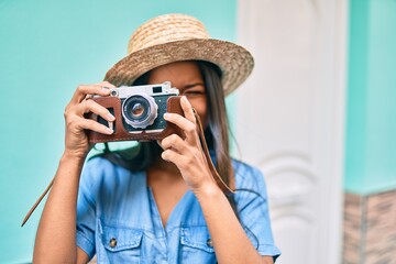 Young latin tourist girl on vacation smiling happy using vintage camera at the city.