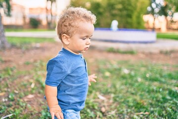 Cute and happy little boy having fun at the park on a sunny day. Beautiful blonde hair male toddler playing outdoors