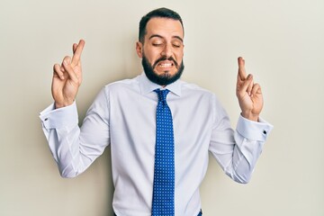 Young man with beard wearing business tie gesturing finger crossed smiling with hope and eyes closed. luck and superstitious concept.