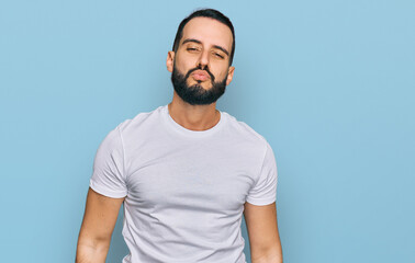 Young man with beard wearing casual white t shirt looking at the camera blowing a kiss on air being lovely and sexy. love expression.