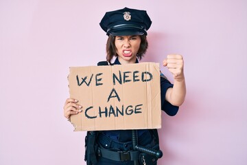 Young beautiful woman wearing police uniform holding we need a change banner annoyed and frustrated shouting with anger, yelling crazy with anger and hand raised