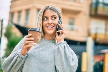 Young blonde girl talking on the smartphone and drinking coffee at the city