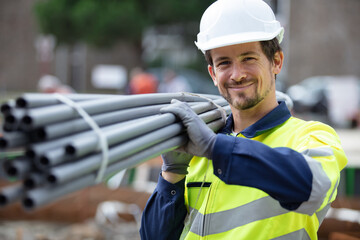 happy construction worker on site holding pipe - Powered by Adobe