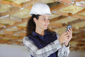 female builder using smartphone inside property under renovation