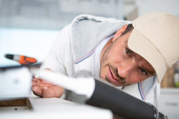 young repairman working at the kitchen with silicone gun