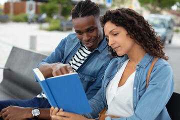 young couple reading book on bench