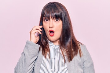 Young plus size woman having conversation talking on the smartphone scared and amazed with open mouth for surprise, disbelief face