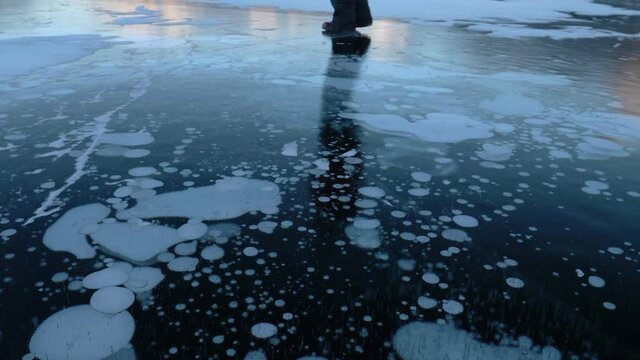 Methane bubbles frozen in Arctic lake surface ice - Climate change raises methane CH4 gas under an Arctic circle lake's solid surface. Permafrost is a climate emergency tipping point. Feet on ice.