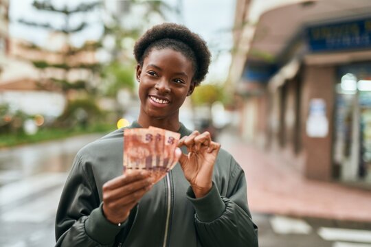 Young african american girl smiling happy counting south africa rands at the city.