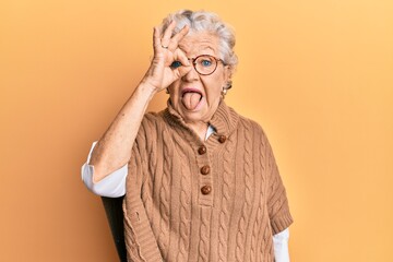 Senior grey-haired woman doing ok positive gesture on eye sticking tongue out happy with funny expression.