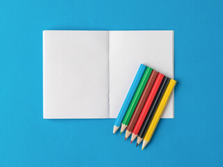 Six colored pencils on an open notebook on a blue background.