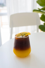 A refreshing glass of iced americano coffee mixed with orange juice decorated with rosemary and sliced orange, on the white background. portrait size.