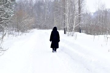 A woman in a black fur coat walks the road covered with snow.