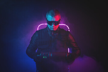 Man in the black jacket and glasses with a secret weapon container in the neon lights concept.