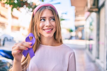 Young caucasian girl smiling happy holding purple ribbon walking at the city.
