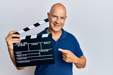 Middle age bald man holding video film clapboard smiling happy pointing with hand and finger