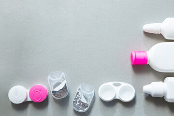 Contact lenses and accessories flat lay on a gray background. Composition with solution bottles and lens containers with copy space