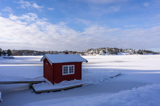 Small Wooden Cabin Little House In The Middle Of The Water Of Lake Or Sea Bay. Bath House Or Sauna Near The Shores Of The Baltic Sea In Winter Sunny Day. Typical Traditional Red House In Scandinavia. 