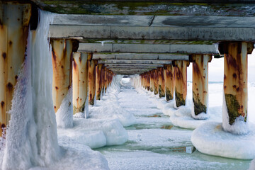 Frozen sea under the pier with rusty pillars