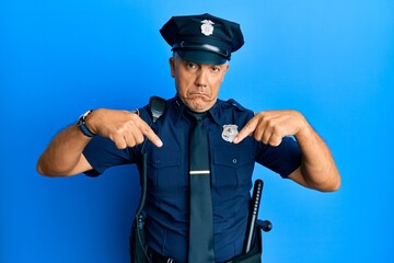 Handsome middle age mature man wearing police uniform pointing down looking sad and upset, indicating direction with fingers, unhappy and depressed.