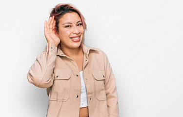 Hispanic woman with pink hair wearing casual clothes smiling with hand over ear listening an hearing to rumor or gossip. deafness concept.