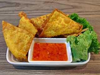 Deep fried pork wontons with sweet chilli sauce on wooden table.