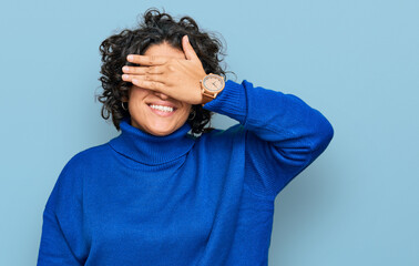 Fototapeta na wymiar Young hispanic woman with curly hair wearing turtleneck sweater smiling and laughing with hand on face covering eyes for surprise. blind concept.