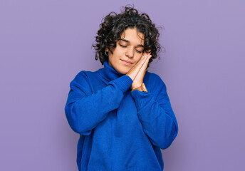 Young hispanic woman with curly hair wearing turtleneck sweater sleeping tired dreaming and posing with hands together while smiling with closed eyes.