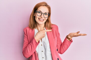 Young caucasian woman wearing business style and glasses amazed and smiling to the camera while presenting with hand and pointing with finger.