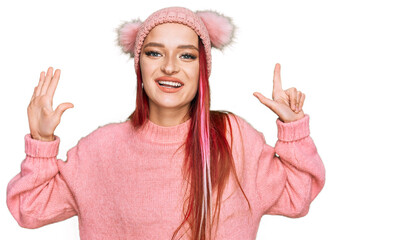 Young caucasian woman wearing casual clothes and wool cap showing and pointing up with fingers number seven while smiling confident and happy.