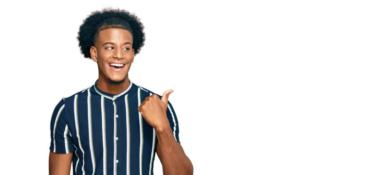 African american man with afro hair wearing casual clothes smiling with happy face looking and pointing to the side with thumb up.