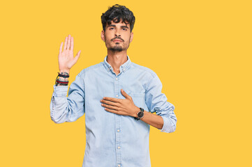 Young hispanic man wearing casual clothes swearing with hand on chest and open palm, making a...