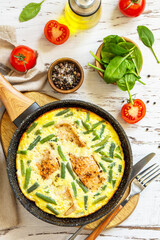 Healthy breakfast or diet lunch. Rustic omelet (omelette, Scrambled)  with salmon fillet and green beans in a frying pan on a white kitchen wooden table. Top view flat lay.