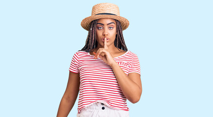 Young african american woman with braids wearing summer hat asking to be quiet with finger on lips....