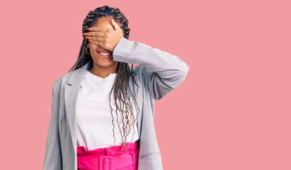 Young african american woman with braids wearing business clothes smiling and laughing with hand on face covering eyes for surprise. blind concept.