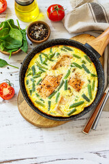 Healthy breakfast or diet lunch. Rustic omelet (omelette, Scrambled)  with salmon fillet and green beans in a cast iron pan on a white kitchen wooden table. Copy space.