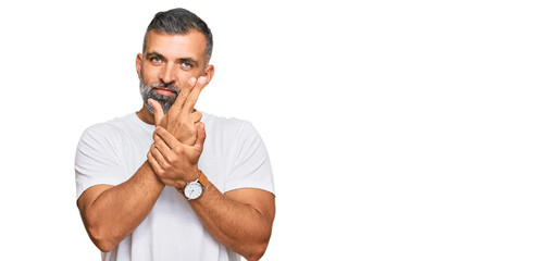 Middle age handsome man wearing casual white tshirt holding symbolic gun with hand gesture, playing killing shooting weapons, angry face