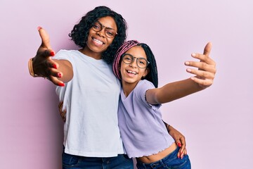 Beautiful african american mother and daughter wearing casual clothes and glasses looking at the...