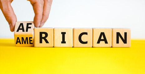 African american symbol. Businessman turns cubes with words 'african american'. Beautiful yellow table, white background. Business and african american concept. Copy space.