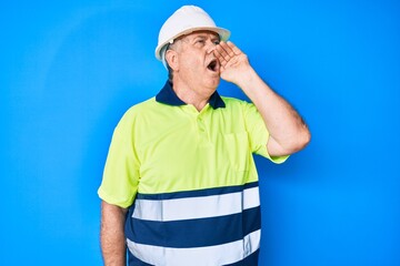 Senior grey-haired man wearing worker reflective t shirt and hardhat shouting and screaming loud to side with hand on mouth. communication concept.