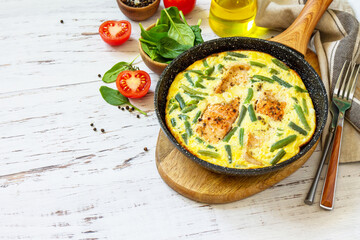 Healthy breakfast or diet lunch. Rustic omelet (omelette, Scrambled)  with salmon fillet and green beans in a cast iron pan on a white kitchen wooden table. Copy space.