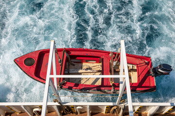 Red lifeboat hanging over sea on the side of a ferry.