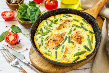 Healthy breakfast or diet lunch. Rustic omelet (omelette, Scrambled)  with salmon fillet and green beans in a cast iron pan on a white kitchen wooden table.