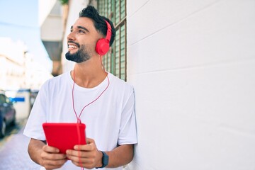 Young arab man smiling happy using headphones and touchpad at the city.
