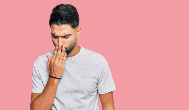 Young man with beard wearing casual grey tshirt bored yawning tired covering mouth with hand. restless and sleepiness.