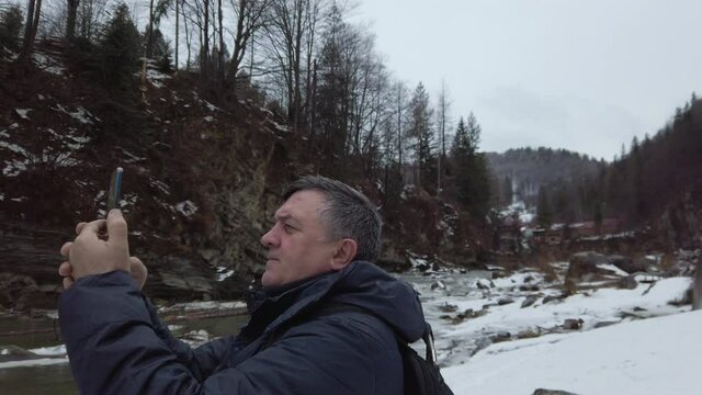 Middle-aged hiker photographing the mountains in winter from a mobile phone. Adult man enjoying traveling at the rocky terrain