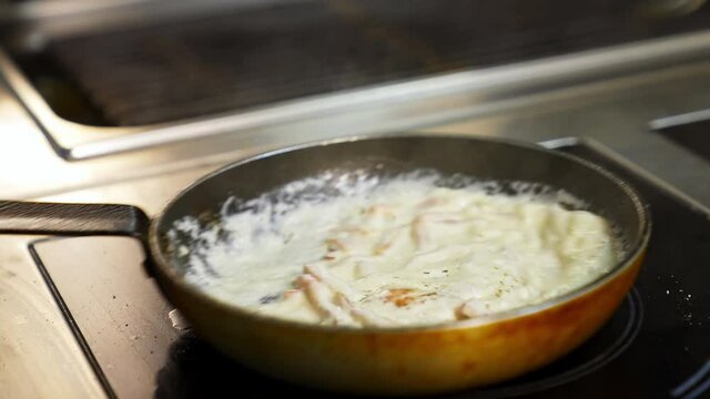 Cooking delicious meal in white sauce. Chef is cooking tasty dish in a frying pan in a restaurant. Close-up.