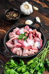 Raw uncooked Bird chicken giblets gizzards, stomachs in a pan. Black wooden background. Top view