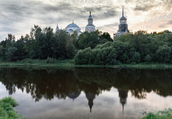 Fototapeta na wymiar View of the Orthodox Cathedral on the river bank. Landscape with a view of the river, trees and reflection in the water in the evening light at sunset